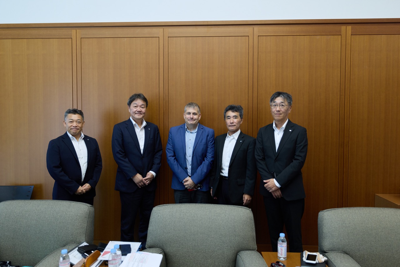 Four executives and the author stand in a conference room facing the camera.