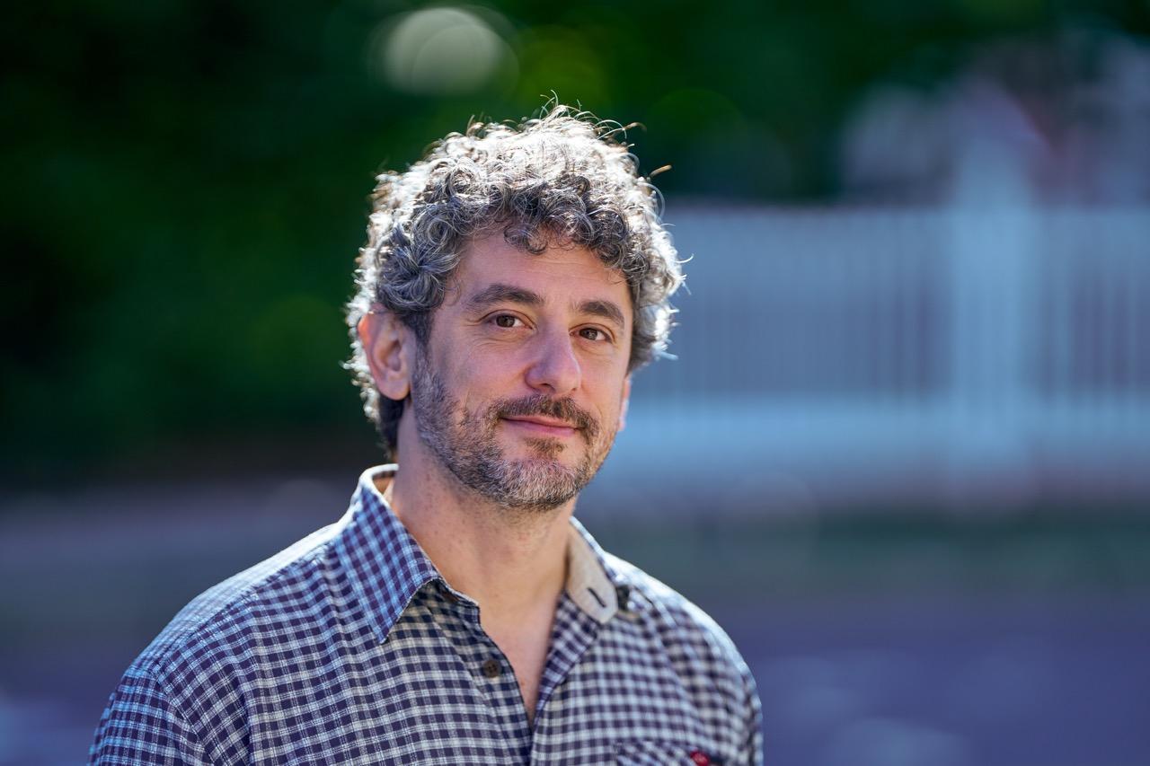 A man standing outside with hair backlit and green background.