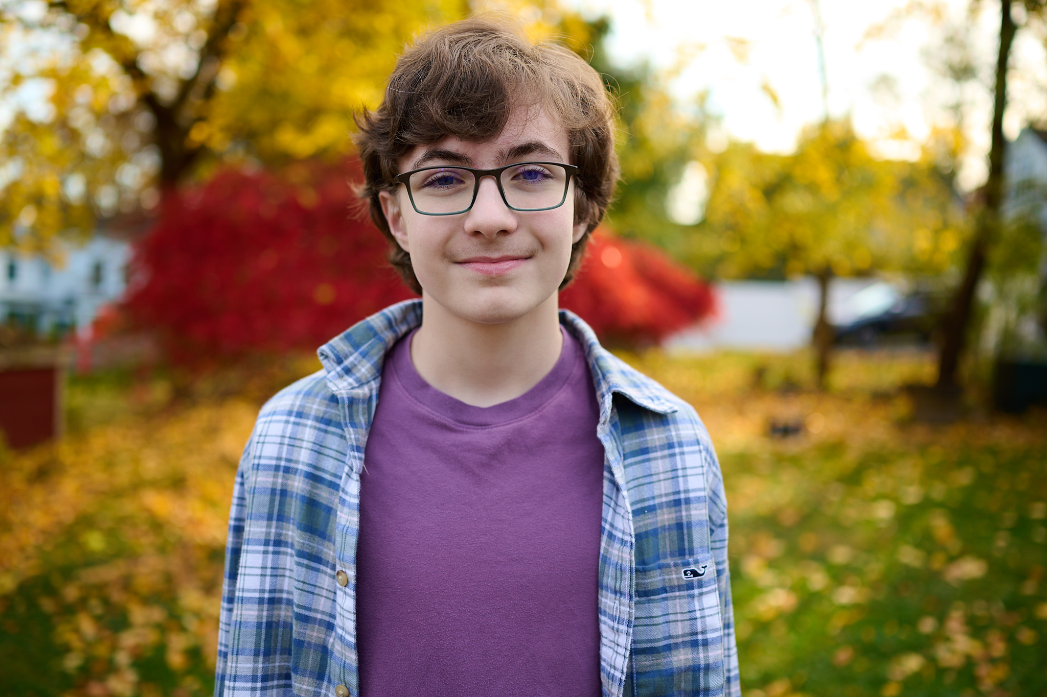 A portrait of a teenage boy outside in the fall with yellow and red folliage behind him.